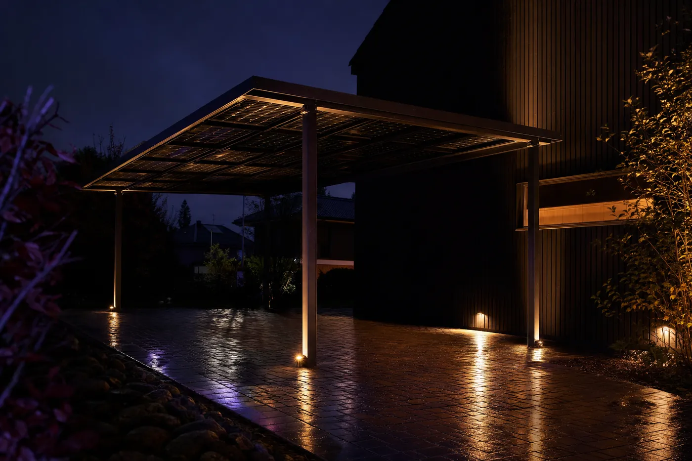 Carport mit Photovoltaikdach neben einem modernen Haus bei Nacht